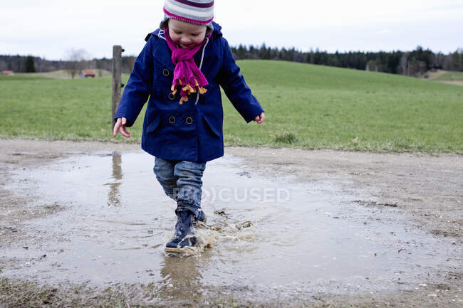 Female toddler wearing rubber boots splashing in puddle — Stock Photo