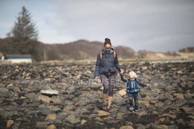 Madre e hijo tomados de la mano caminando sobre rocas - foto de stock