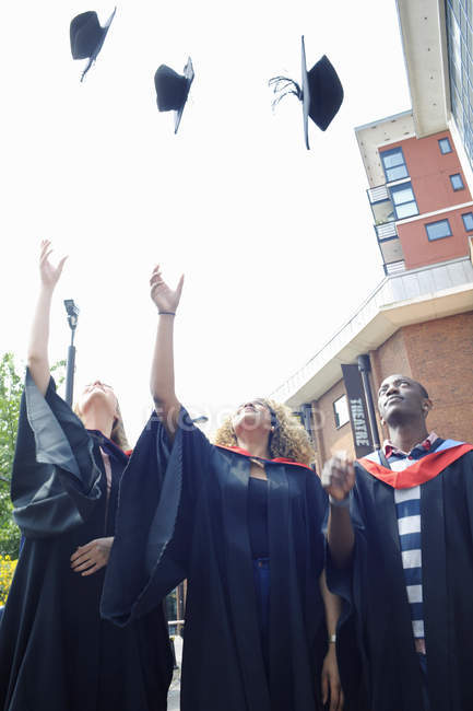 Three college students throwing graduation caps mid air — Stock Photo