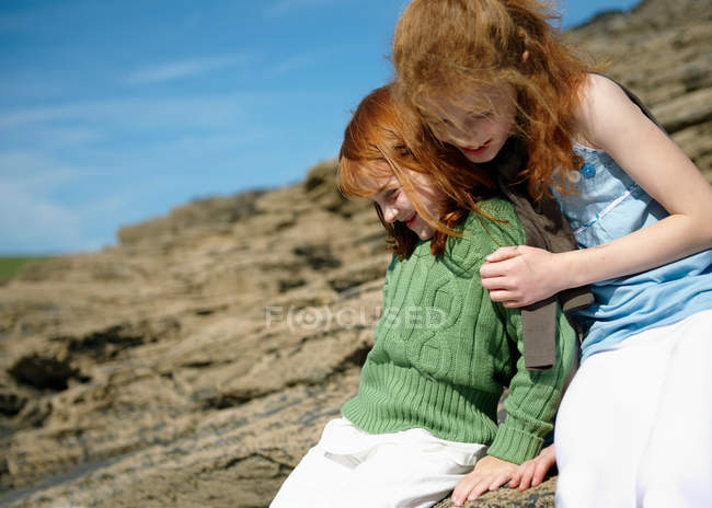 Girl hugging young sister on rocks — Stock Photo