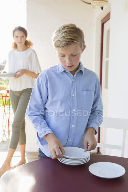 Boy preparing plates on patio table — Stock Photo