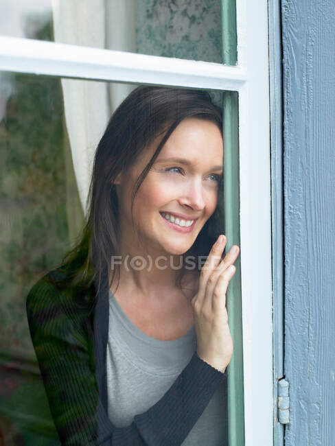 Жінка дивиться крізь вікно, посміхаючись — стокове фото