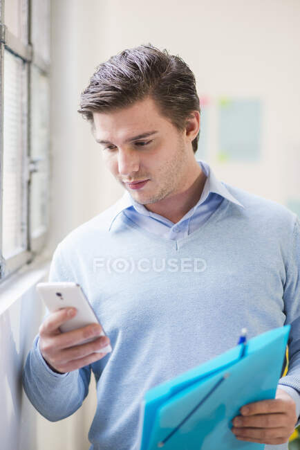 Молодой бизнесмен читает тексты на смартфоне в офисе — стоковое фото