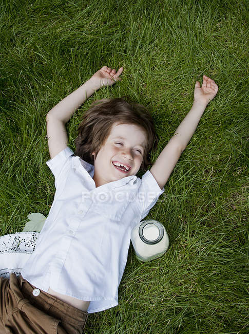 Хлопчик лежить на траві з піднятими руками і сміятися — стокове фото