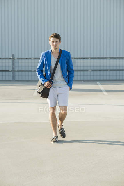 Young man with shoulder bag strolling across empty parking lot — Stock Photo