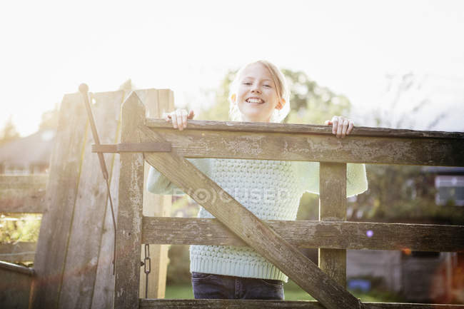 Girl looking over wooden gate in countryside garden — Stock Photo