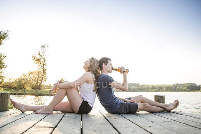 Junges Paar entspannt auf Steg, Rücken an Rücken sitzend — Stockfoto