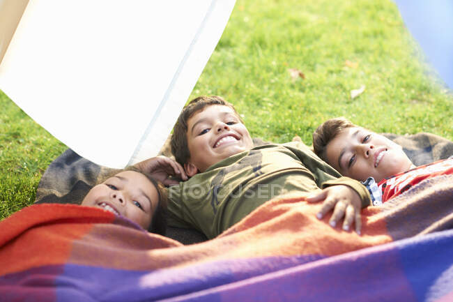 Menina e dois irmãos deitados no jardim envolto em cobertor — Fotografia de Stock