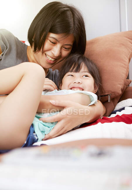 Jovem mãe chinesa e filha deitada no sofá assistindo a televisão juntos em casa — Fotografia de Stock