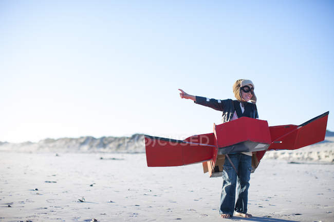 Мальчик стоит с игрушечным самолетом и указывает на пляж — стоковое фото