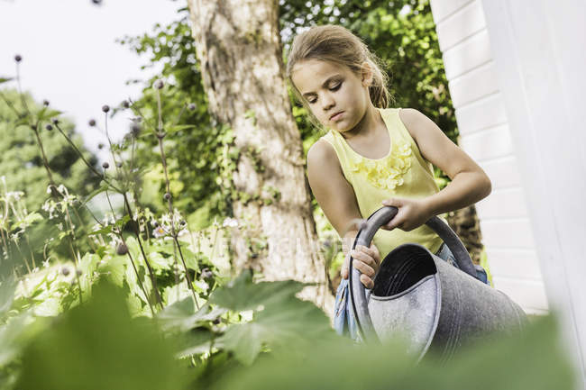 Девушка концентрируется, поливая растения в саду — стоковое фото
