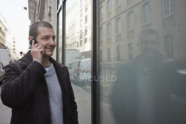 Mid adulto homem falando no smartphone enquanto janela de compras — Fotografia de Stock