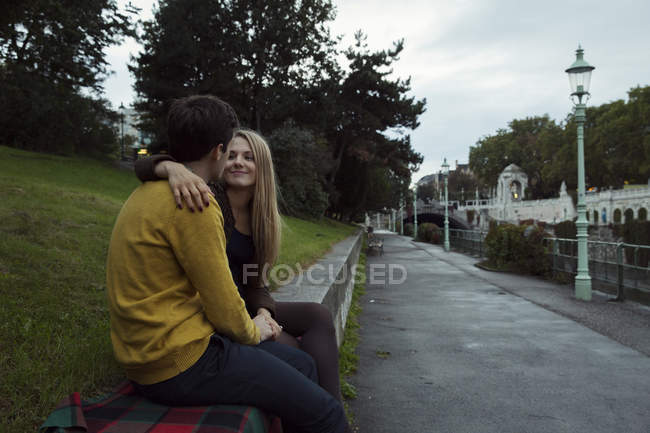 Young couple sitting face to face on park wall — Stock Photo