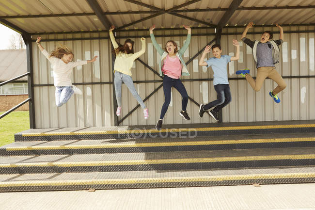 П'ять хлопчиків і дівчат стрибають середнє повітря на трибуні стадіону — стокове фото