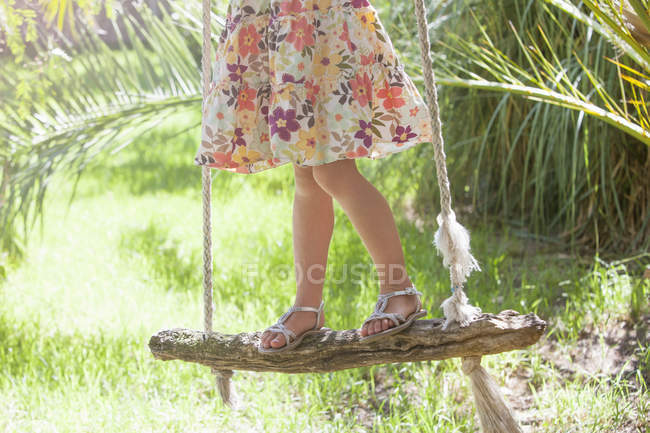 Waist down cropped shot of girl standing on tree swing in garden — Stock Photo