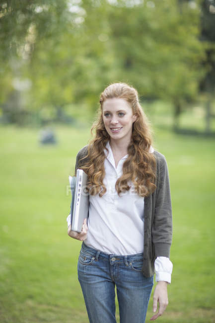 Jeune femme portant un ordinateur portable et marchant dans le parc — Photo de stock