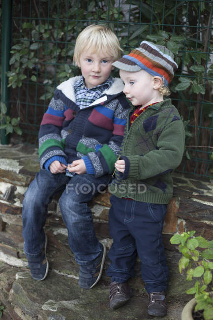 Preschooler brothers sitting in garden on stone wall together outdoors — Stock Photo