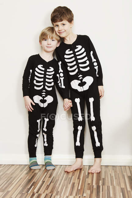 Dos chicos vestidos con trajes de esqueleto mirando en cámara contra pared blanca - foto de stock