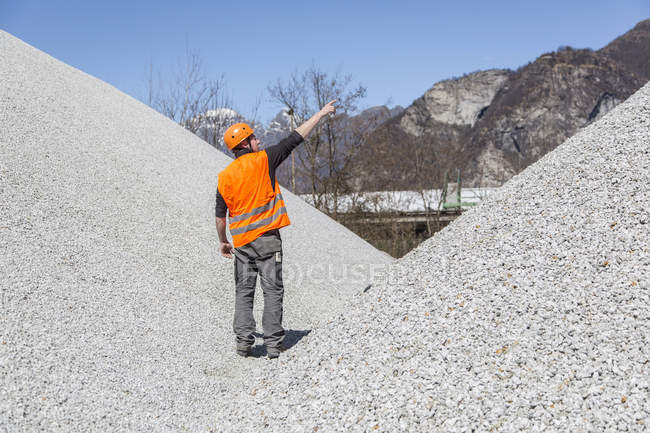 Quarry worker pointing from gravel mounds at quarry — Stock Photo