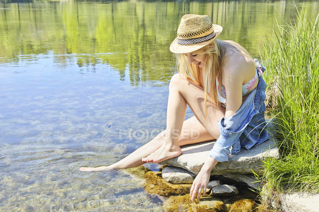 Jeune femme assise sur des rochers près de l'eau — Photo de stock
