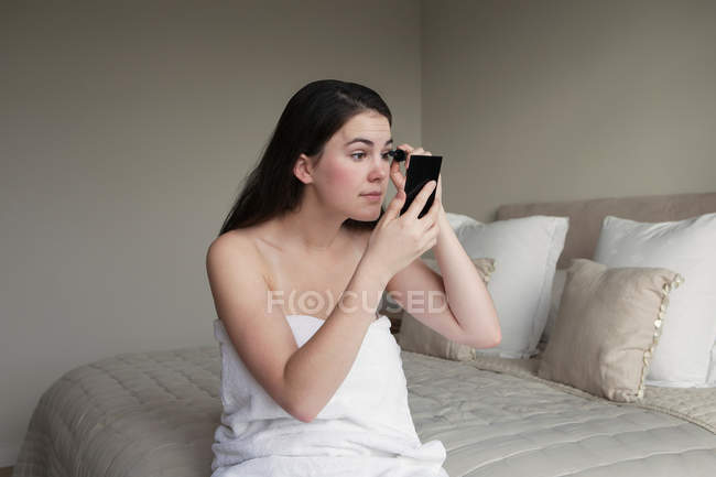 Woman applying mascara on bed — Stock Photo