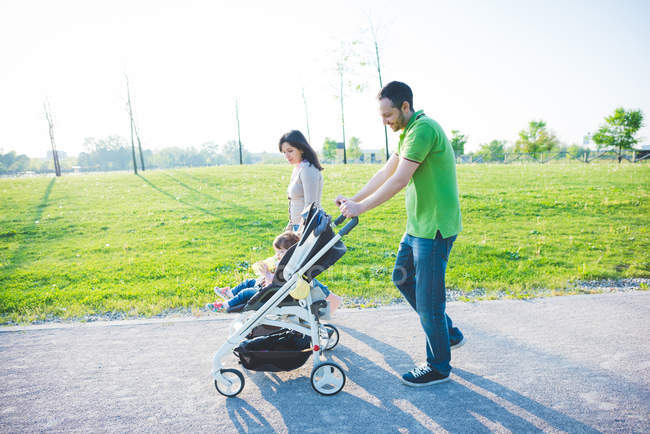 Mid adult couple and toddler daughter in pushchair strolling in park — Stock Photo