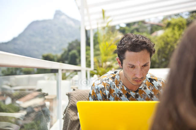Homem adulto médio sentado na varanda, usando laptop — Fotografia de Stock