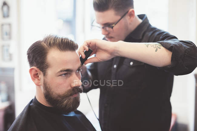 Парикмахер с помощью ножниц для стрижки волос клиента — стоковое фото