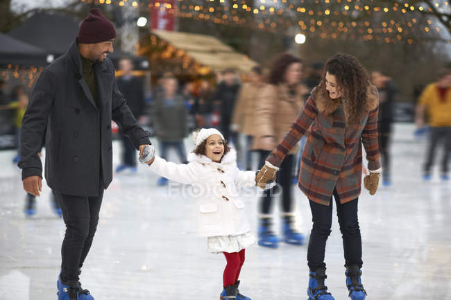 Chica sosteniendo padres manos patinaje sobre hielo, sonriendo - foto de stock