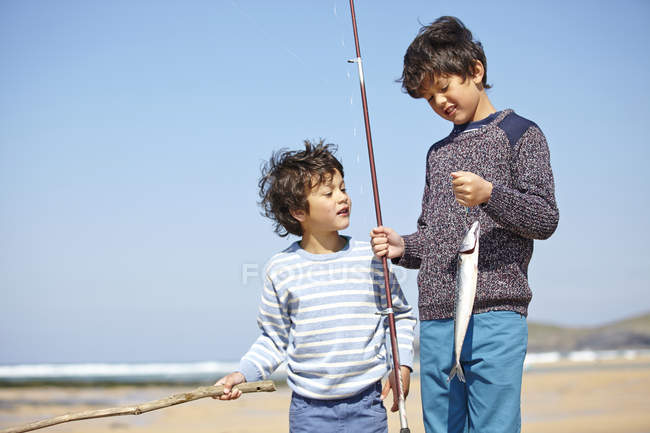 Dois meninos de pé juntos, segurando vara de pesca e peixe — Fotografia de Stock
