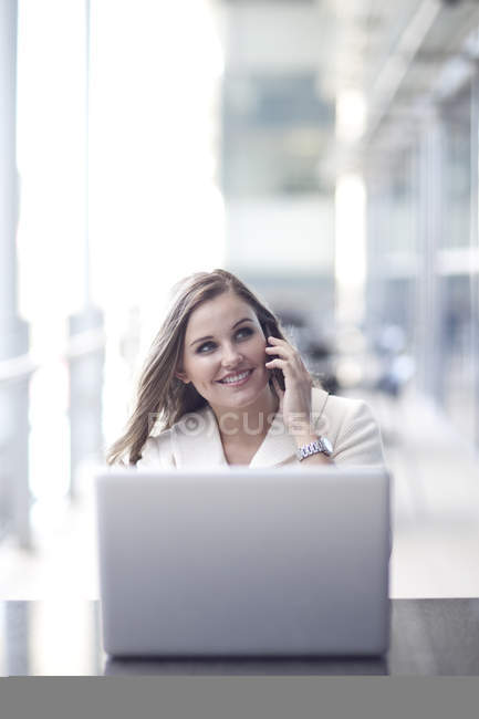 Young businesswoman using laptop and chatting on smartphone in conference centre — Stock Photo