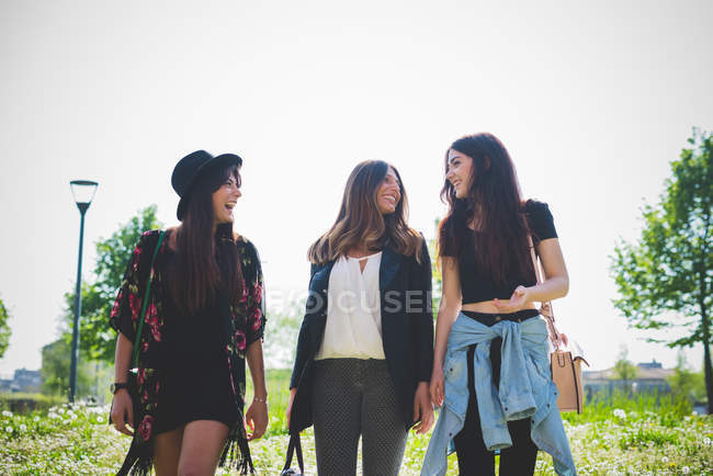Three young women chatting while strolling in park — Stock Photo