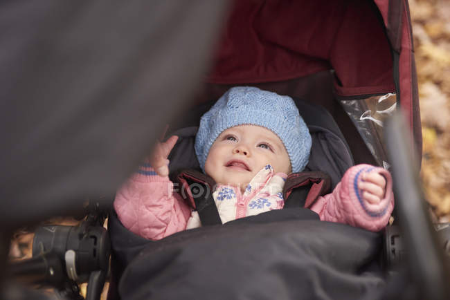 Bebé niña con sombrero azul mirando hacia arriba desde el carro de bebé - foto de stock