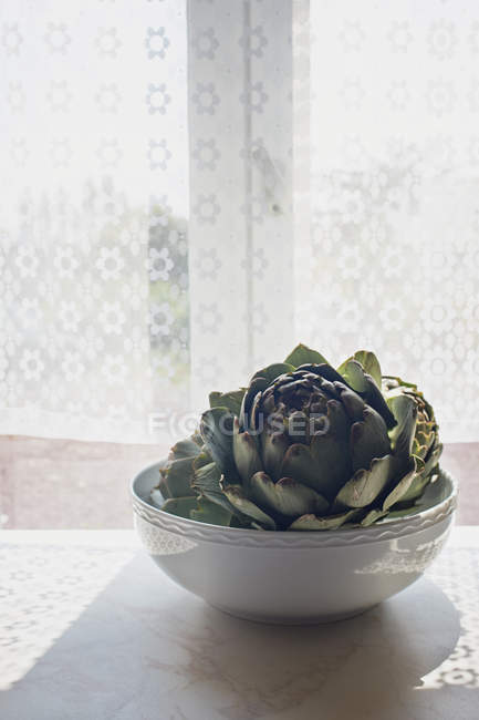 Artichoke in a bowl on sunlit windowsill — Stock Photo