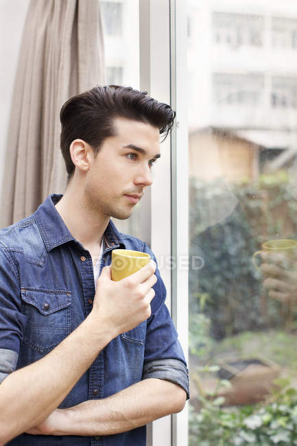 Portrait of young man gazing through patio door — Stock Photo