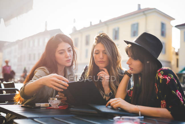 Три молодые женщины смотрят на цифровые планшеты в кафе на тротуаре — стоковое фото
