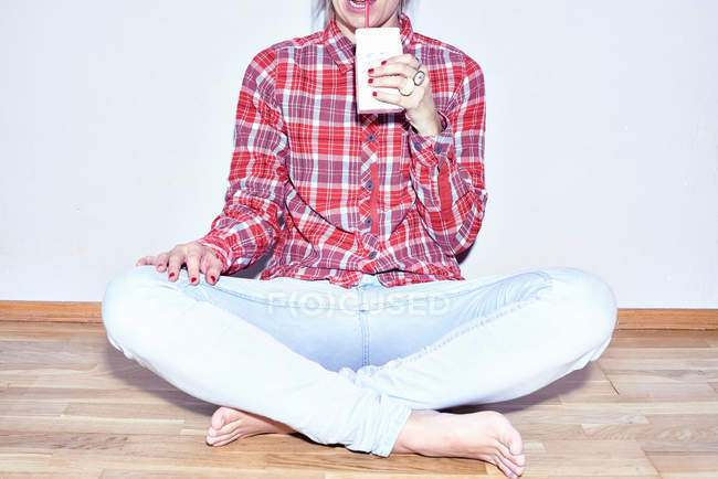 Vue recadrée de la jeune femme assise sur le sol et buvant du jus — Photo de stock