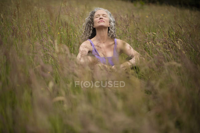 Femme mûre assise dans l'herbe longue méditant — Photo de stock