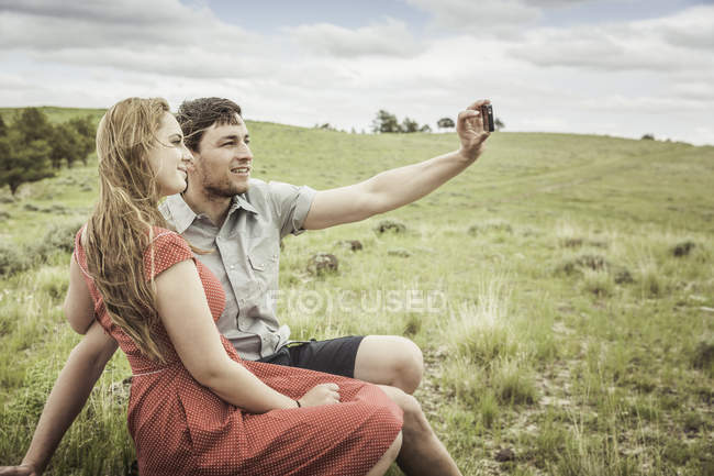 Coppia giovane seduta sulla cima della collina a scattare selfie per smartphone, Cody, Wyoming, USA — Foto stock