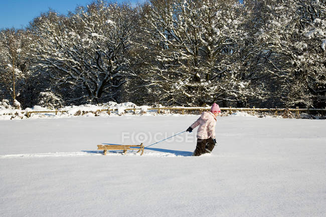 Young girl pulling sledge in snow — Stock Photo