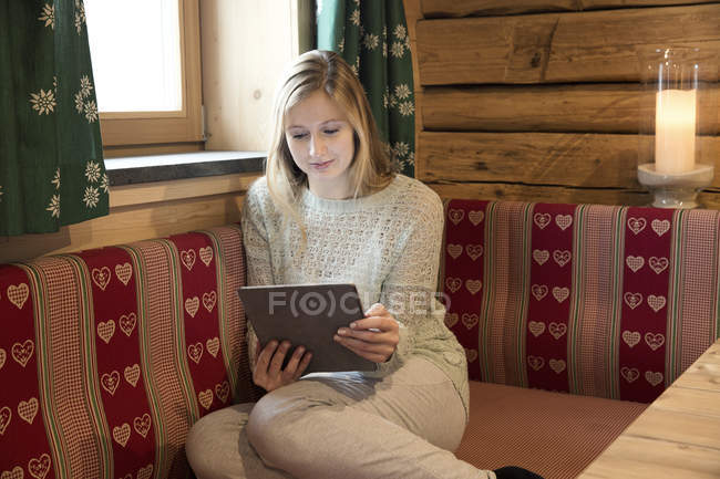 Mujer joven leyendo tableta digital en cabaña de madera - foto de stock