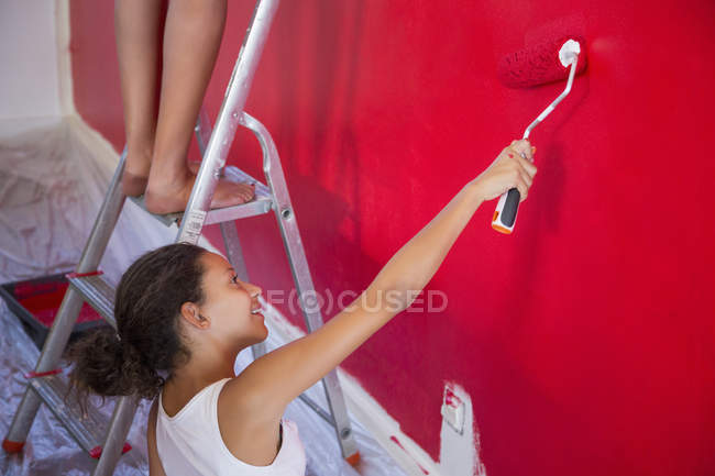 Menina e mãe pintura parede vermelha com rolo de pintura — Fotografia de Stock