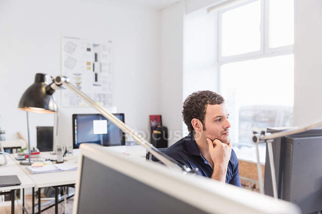 Hombre adulto en la oficina usando la mano de la computadora en la barbilla - foto de stock