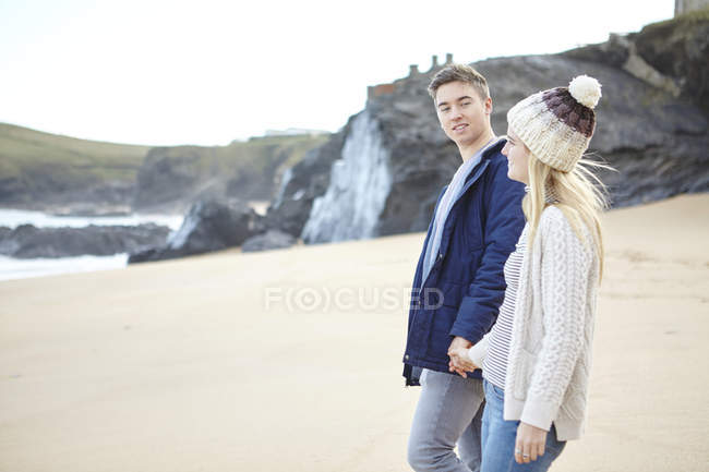 Молодая пара, прогуливающаяся рука об руку на пляже, Константин Бей, Корнуолл, Великобритания — стоковое фото