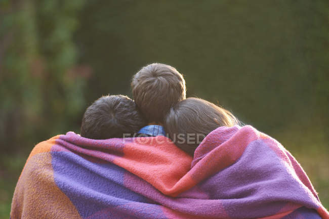Hermanos envueltos en manta en jardín - foto de stock