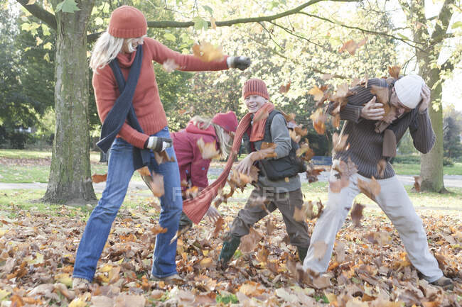 Family fooling around in park, throwing autumn leaves — Stock Photo