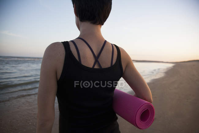 Vue arrière de la femme adulte moyenne se préparant pour le yoga sur la plage au coucher du soleil — Photo de stock