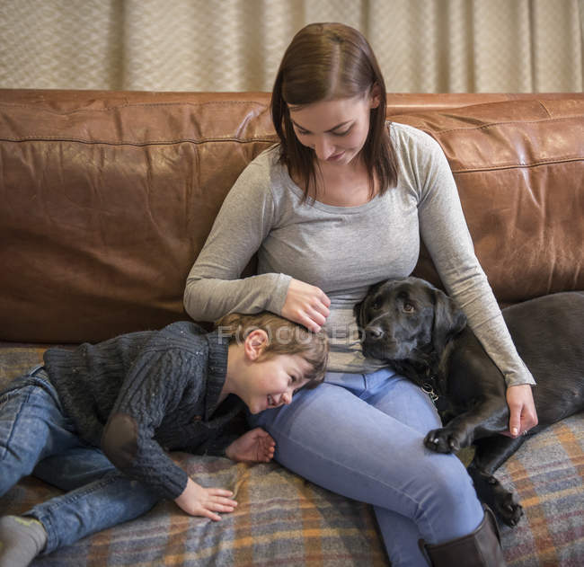 Мать и сын отдыхают дома на диване с домашним лабрадором — стоковое фото