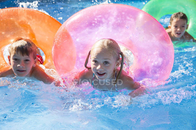 Three children swimming with inflatable rings in garden swimming pool — Stock Photo