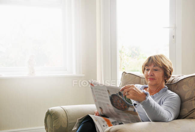 Mujer mayor sentada en sillón leyendo revista - foto de stock